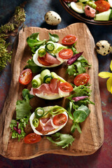 Easter breakfast with egg halves with prosciutto ham and vegetables on wooden board top view