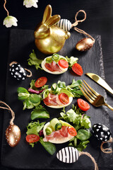 Top view of Easter breakfast with egg halves with prosciutto ham and vegetables on black board