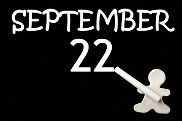A small white plasticine man writing the date 22 September on a black board. Business concept. Education concept.
