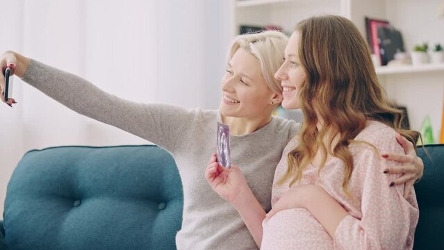Expecting lesbian parents taking a selfie with ultrasound image of their baby