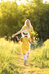 Mother and little daughter having fun in summer meadow with yellow flowers. Happy family on summer....