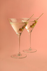 two martini glasses with olives on pink background