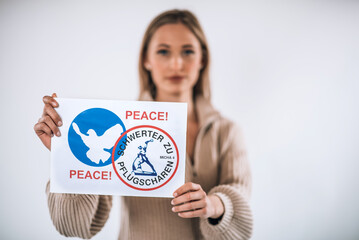 Eine junge, blonde Frau demonstriert für den Frieden und hält ein Plakat mit Friedenstaube und...