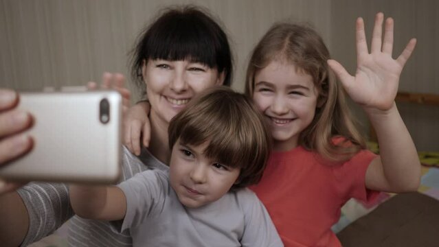 Portrait Mother and Kids Kissing on Camera. Happy Mother With Her Kids are Making Selfie or Video Call to Father or Relatives in Bed. Technology, New Generation Parenthood. Video Call Family Selfie.