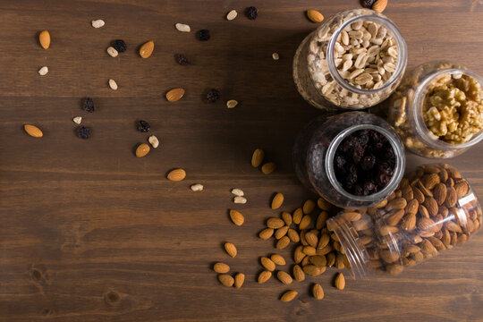 Bodeg&oacute;n de envases con frutos secos, nueces, almendras, man&iacute; y pasas de uva. Frascos transparentes con tapas amarillas. Naturaleza muerta. 