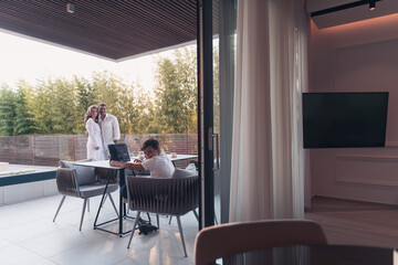 Happy elderly couple resting on the balcony of a luxury house while their son using a tablet. Selective focus