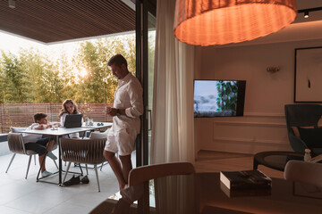 An elderly couple enjoys the terrace of a luxury house with their son during the holidays....
