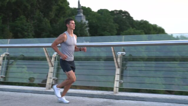 athletic muscular man in sportswear running in the morning on glassy bridge, run