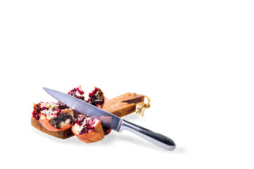 A ripe pomegranate, grains, on a cutting board with a knife and juicer. White background.