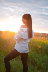 young woman in baldric on the summer field on sunset or sunrise. peaceful calm female. trendy clothes