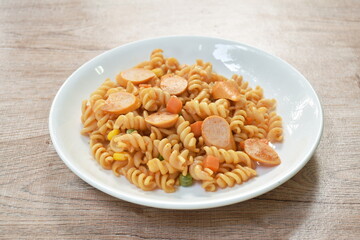 stir fried Gemelli Italian pasta with slice pork sausage and garden pea with corn in ketchup on plate