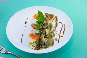 Caprese salad with tomatoes, mozzarella and basil. Red and orange tomatoes with white cheese and sauce. Portion of food on a plate in a restaurant. View from above. Delicious healthy food.