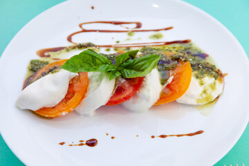 Caprese salad with tomatoes, mozzarella and basil. Red and orange tomatoes with white cheese and sauce. Portion of food on a plate in a restaurant. View from above. Delicious healthy food.