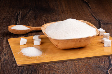 Pieces of white sugar and granulated sugar on a wooden background.