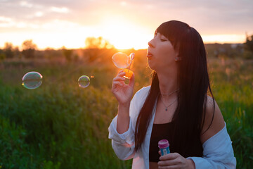 pretty young woman making soap bubbles in summer green field on sunset. happy peaceful time. millennial generation