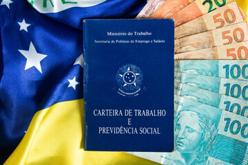 Brazilian document work and social security (Carteira de Trabalho e Previdencia Social) with Brazilian money banknotes and Brazilian flag in the background