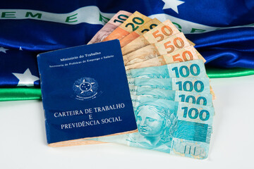 Brazilian document work and social security (Carteira de Trabalho e Previdencia Social) with Brazilian money banknotes and Brazilian flag in the background