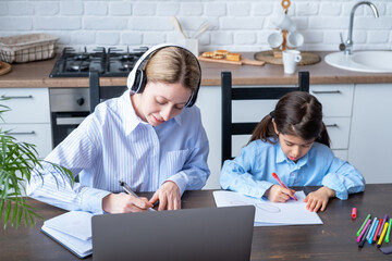 woman in headphone having online lesson education using laptop. kid girl drawing sitting next to her