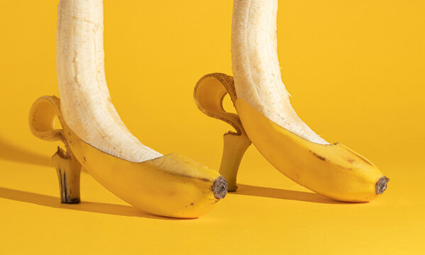 Two bananas on a yellow background peeled to half. Creative minimal surreal concept. Women's shoes and feet.