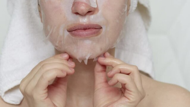 pretty woman is applying a white sheet mask on her face. close up video of bottom part of the face, mouth, nose and neck zone. spa at home. paper sheet facial mask for moisturizing and anti wrinkle.