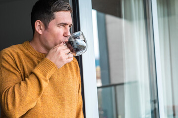 Man in knitted wool sweater drinks tea a cup, relax at home in autumn day. Health care, authenticity, sense of balance and calmness. Fresh air.