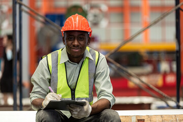 Happy male african american workers wear red helmet working take notes on paperwork sitting in...