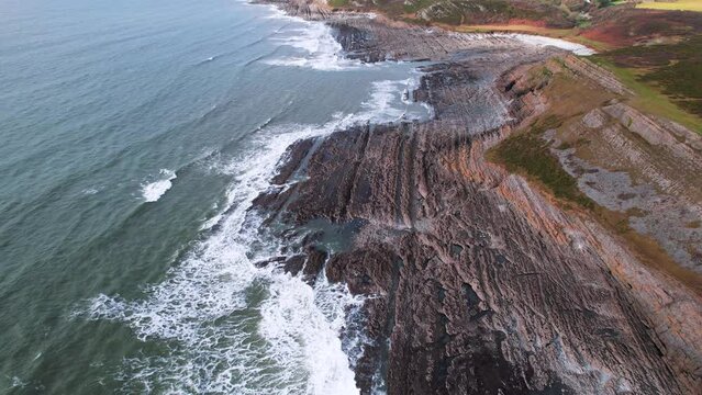AERIAL: Fly towards along textured rocky coastline with crashing waves, Port Eynon Gower, 4k Drone