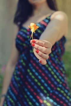 Mujer con flor capuchina naranja en la mano, con vestido colorido