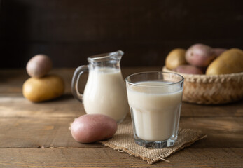 Vegan potato milk in glass and milk jar with raw potatoes on the wooden background in rustic style