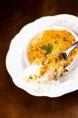 close-up fish casserole on spoon with cheese and crispy breaded and blurred plate