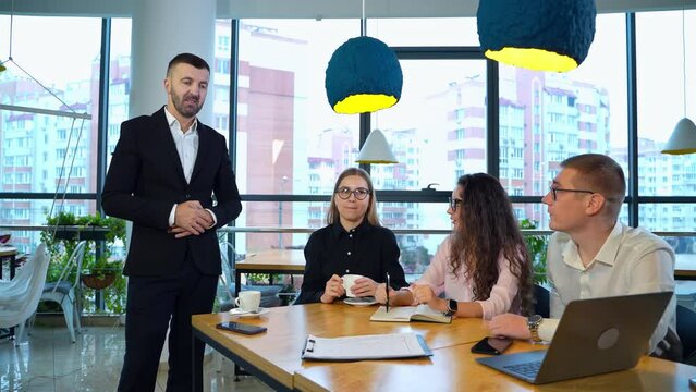 Young women talk to each other not paying attention to the men on both sides from them. Man at the desk gives a speech to somebody else in the room.
