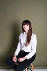 Young beautiful lonely student girl in a white shirt sitting on a green background