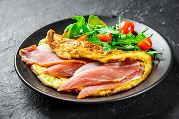 omelette with prosciutto and salad on black plate on Dark grey black slate background