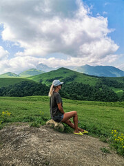 Fototapeta na wymiar A girl on the background of a green landscape of the Aktoprak pass in the Caucasus. Russia June 2021.