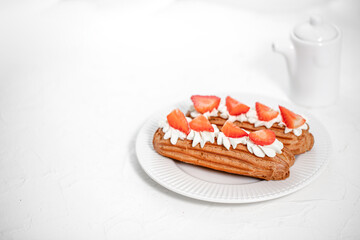 Eclairs with cream and strawberries on a white plate. 