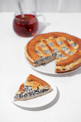 Homemade cake with cottage cheese and poppy seeds and a mug of tea on a white table. 