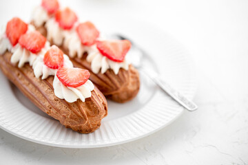 Eclairs with cream and strawberries and a cup of tea on a white plate. 