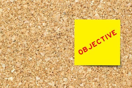 Yellow note paper with word objective on cork board background with copy space
