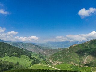 Fototapeta premium The landscape of the green Aktoprak pass in the Caucasus, the road and the mountains under gray clouds. Russia.
