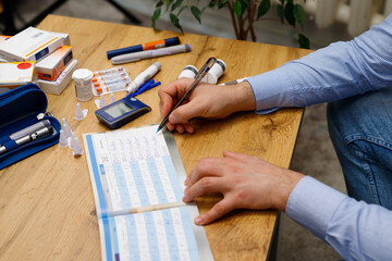 Close up picture of a diary man writing blood glucose level for self-control and monitors, control diabetes.