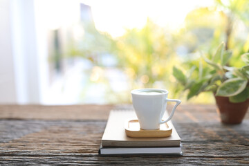 Green tea in white cup with books and plant pot on wooden table