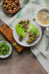Open toasts with baked mini champignons, avocado slices, radish microgreens and cream cheese. Light healthy lunch in a plate on a board with a tablecloth. Minimalistic table setting.