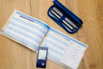 Close up photo of a diabetic diary, glucose meter and pens to note data of measuring blood sugar level, diabetic concept.