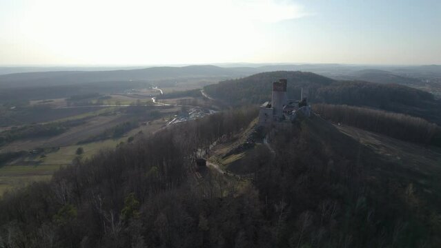 A tracking aerial drone shot of the Chęciny Royal Castle revealing the landscape of the valley. This is located in Poland. It fell into ruin in the 18th century and remains in that state to this day.