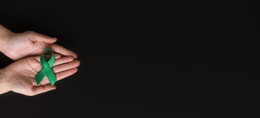 World bipolar day. Adult hands holding green ribbon on black background. Mental health awareness day, Depression, Cerebral palsy. World kidney day.