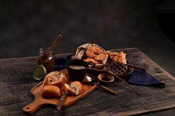 Breakfast Served with Croissants, ham and cheese bread, sausage buns, pies, waffles, pizza, coffee, and chocolate on wooden table with black background, selective focus.