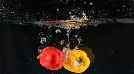 Fototapeta na wymiar Close up of The red, yellow and green bell peppers fell into the water and the water splashed up with black background. Concept for health and vitamins.