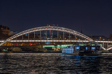 Fototapeta premium Enlightened Pedestrian Bridge at Night in Paris Seine River and Tourists Cruises