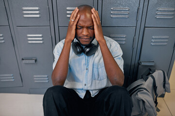 A young black student sits on the floor head in hands, feeling upset at college