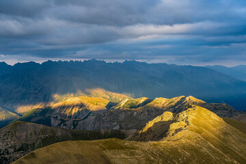 Mountain Ridge Lighted by Golden Sun at Day Under Cloudy and Stormy Sky